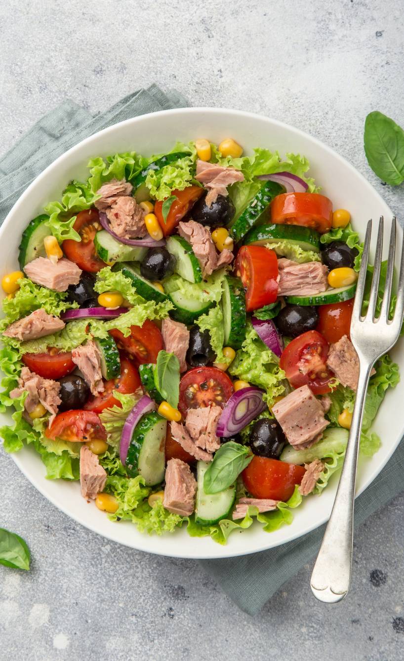 Thunfischsalat mit Mais, Oliven, Gurke, Zwiebel und Tomate auf einem Teller garniert mit frischer Petersilie