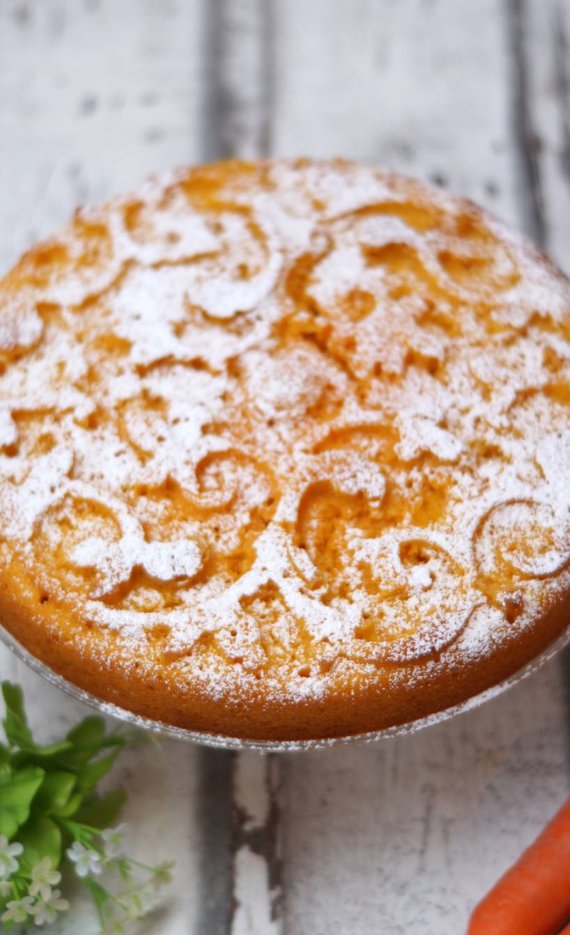 Runder Rüblikuchen Torta di carote mit Ornamentmuster und Puderzucker bestäubt auf einem Kuchenteller