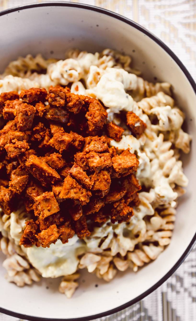 Fusilli Pasta mit veganer Carbonara-Soße getoppt mit Speck aus Tempeh in einer Schüssel
