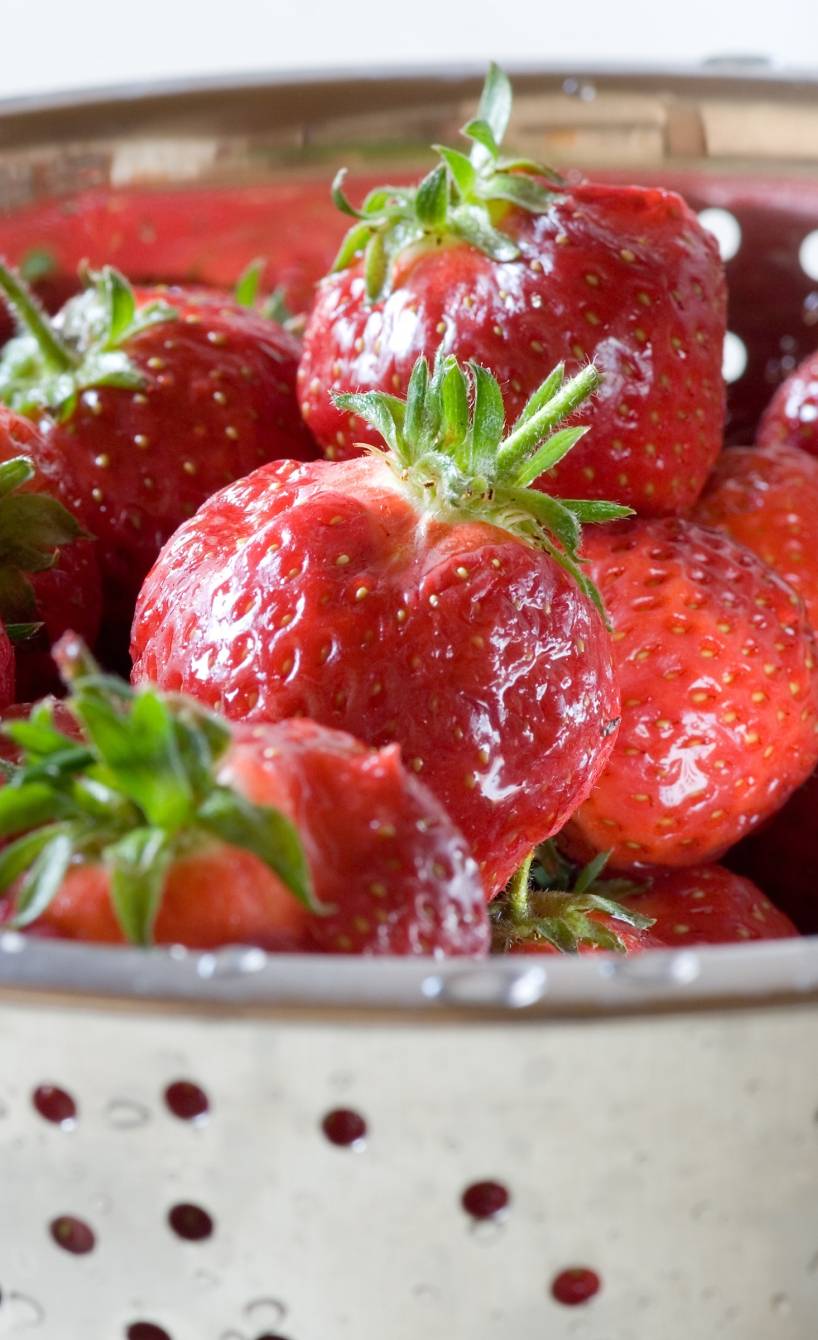 Ganze, nasse Erdbeeren mit Grün in einem silbernen Lochsieb