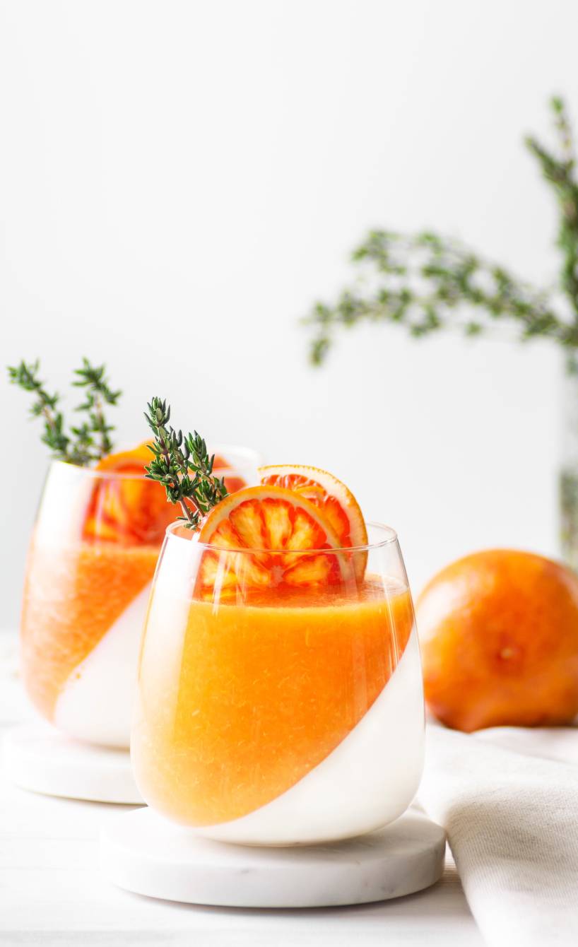 Aperol Spritz Panna Cotta in zwei Gläsern, eine Schicht Panna Cotta eine Schicht Aperol-Fruchtmasse dekoriert mit thymianzweigen 