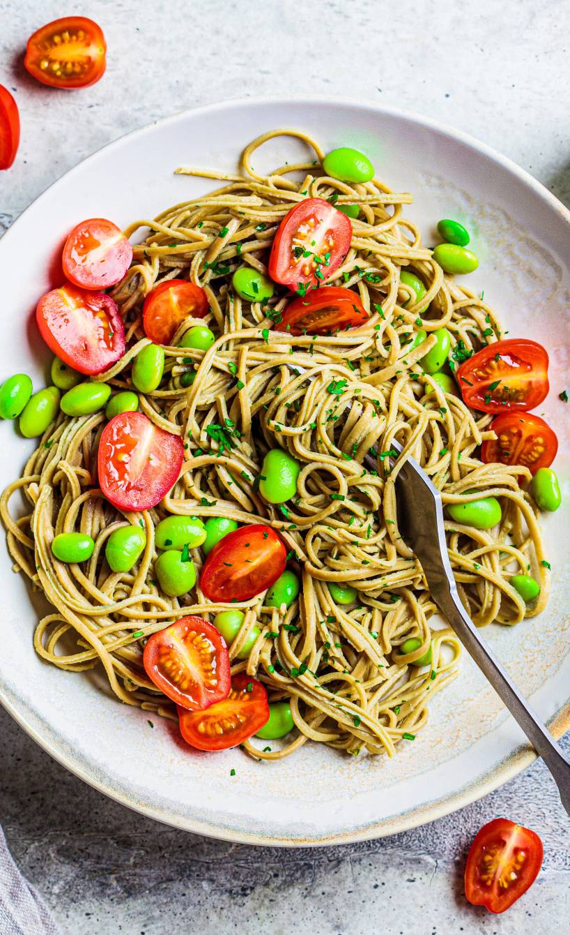 Edamame-Spaghetti auf einem Teller getoppt mit Kirschtomaten und Edamame-Bohnen sowie frischer Petersilie