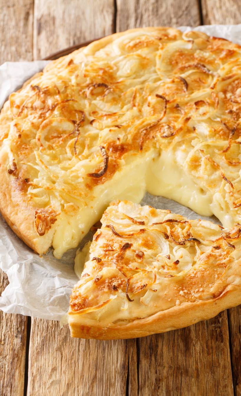 Runde Fugazza angeschnitten mit herauslaufender Füllung aus geschmolzenem Käse getoppt mit Zwiebelringen