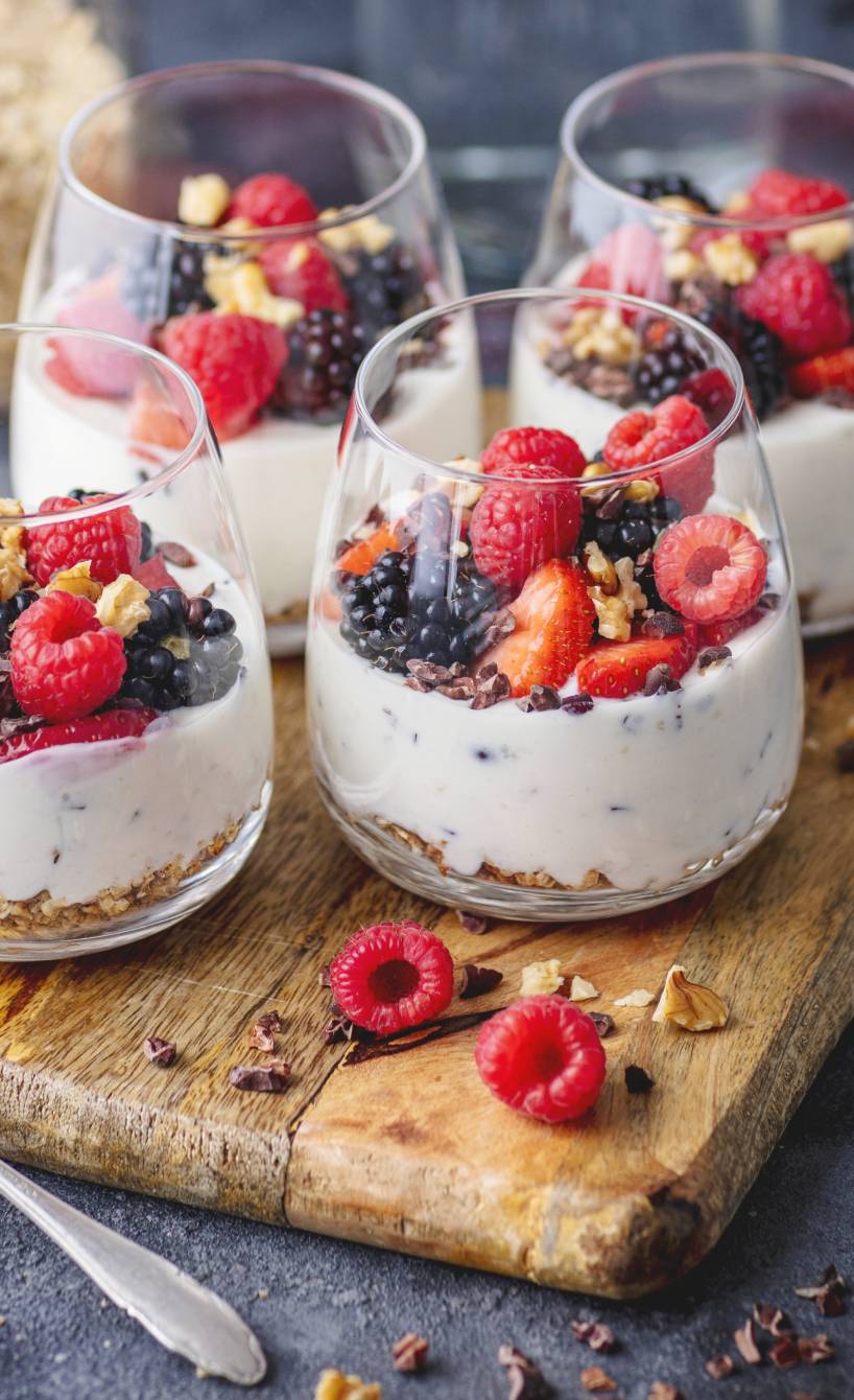Vier Gläser italienisches Stracciatella-Dessert mit Beerentopping auf einem Holzbrett