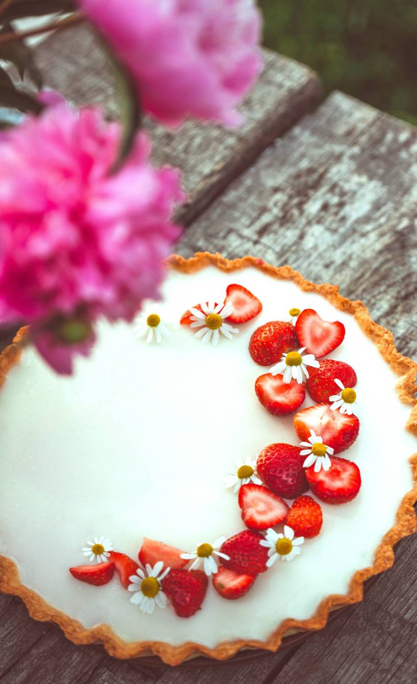 Panna Cotta Tarte auf einem Holztisch dekoriert mit Erdbeerstücken, daneben ein Blumenstrauß