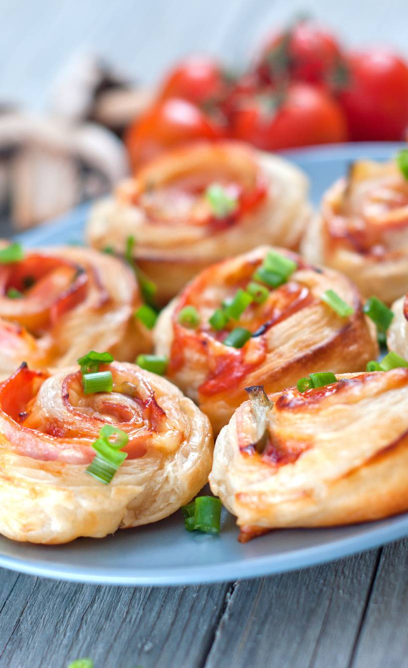 Sieben Pizzaschnecken aus Blätterteig auf einem Teller, Füllung aus Schinken und Käse sichtbar