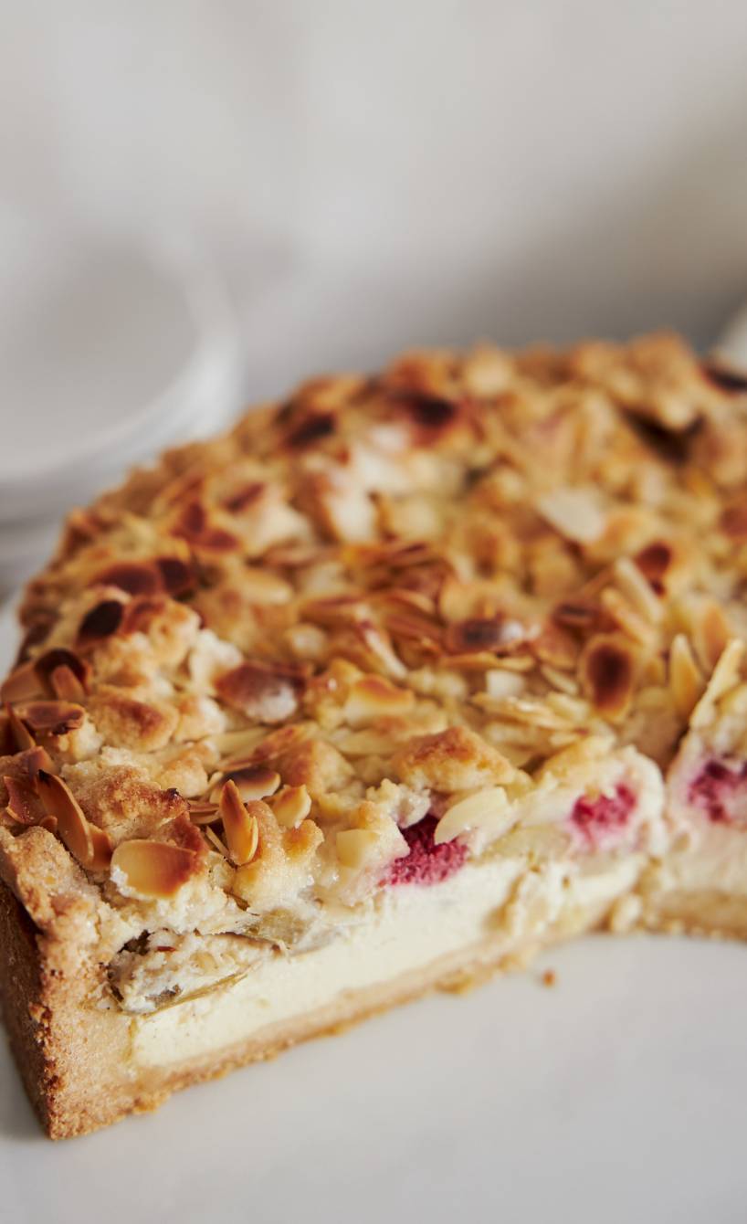 Runder Quark-Rhabarber-Kuchen angeschnitten auf einer Kuchenplatte im close up