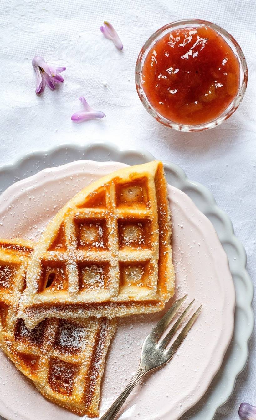 Zerteilte Quark-Waffeln auf zweit Tellern, daneben ein Glas Rhabarberkompott auf einem Tisch