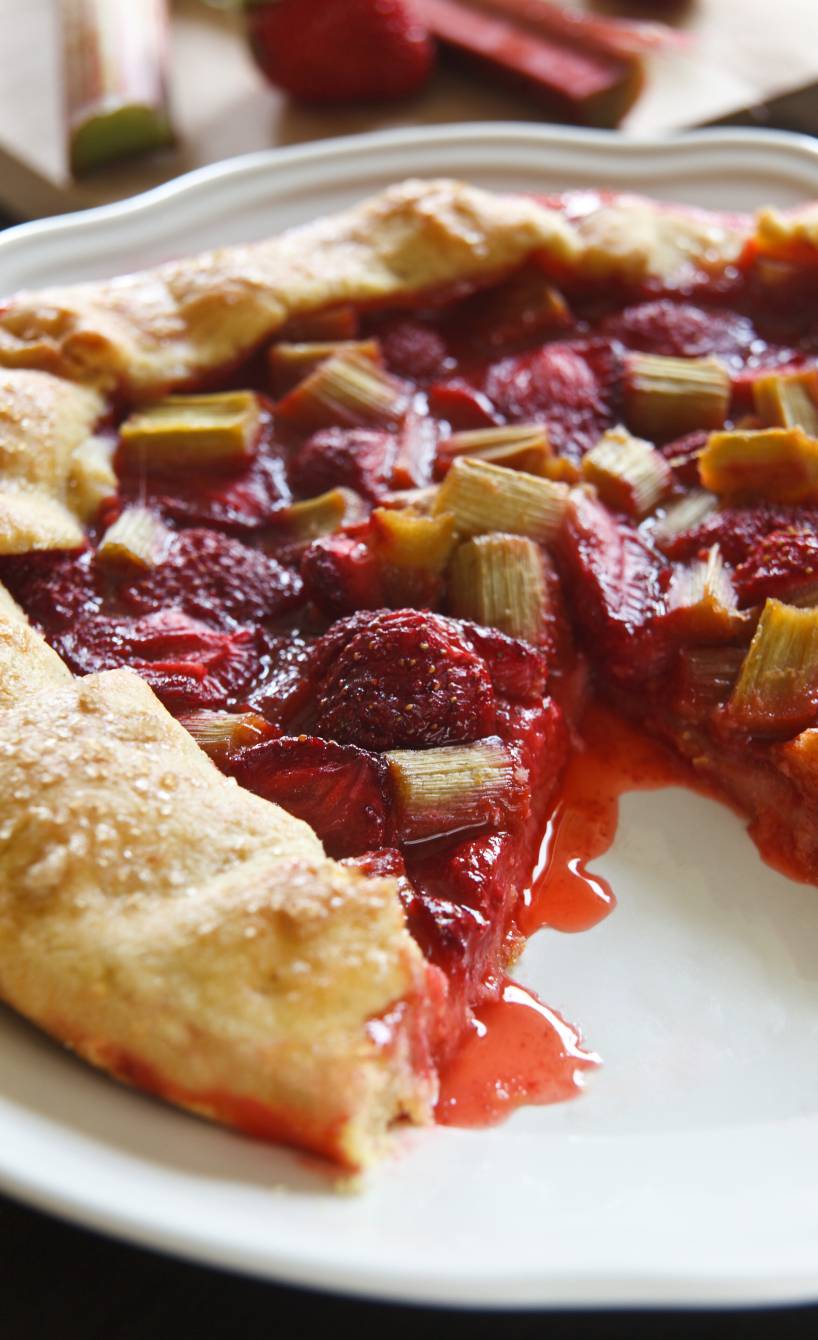 Rhabarber-Ricotta-Crostata mit Erdbeeren angeschnitten auf einem Teller, Saft des Obstes fließt heraus