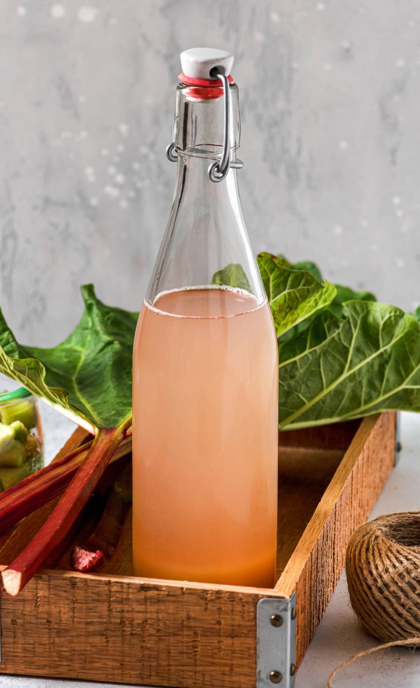 Selbst gemachter Rhabarbersirup abgefüllt in eine Flasche in einer Holzkiste auf einem Tisch