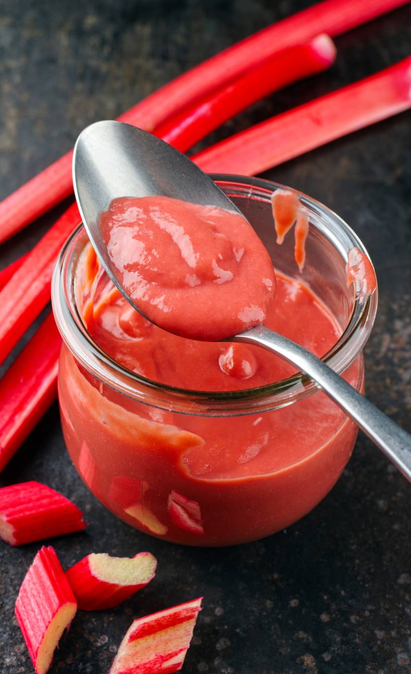 Sehr feine Rhabarber-Konfitüre ohne Stücke in einem Einmachglas, daneben Rhabarberstangen auf einem Tisch