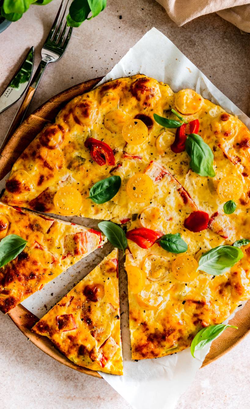 Runde Schüttelpizza angeschnitten auf einem Pizzateller aus Holz getoppt mit frischem Basilikum