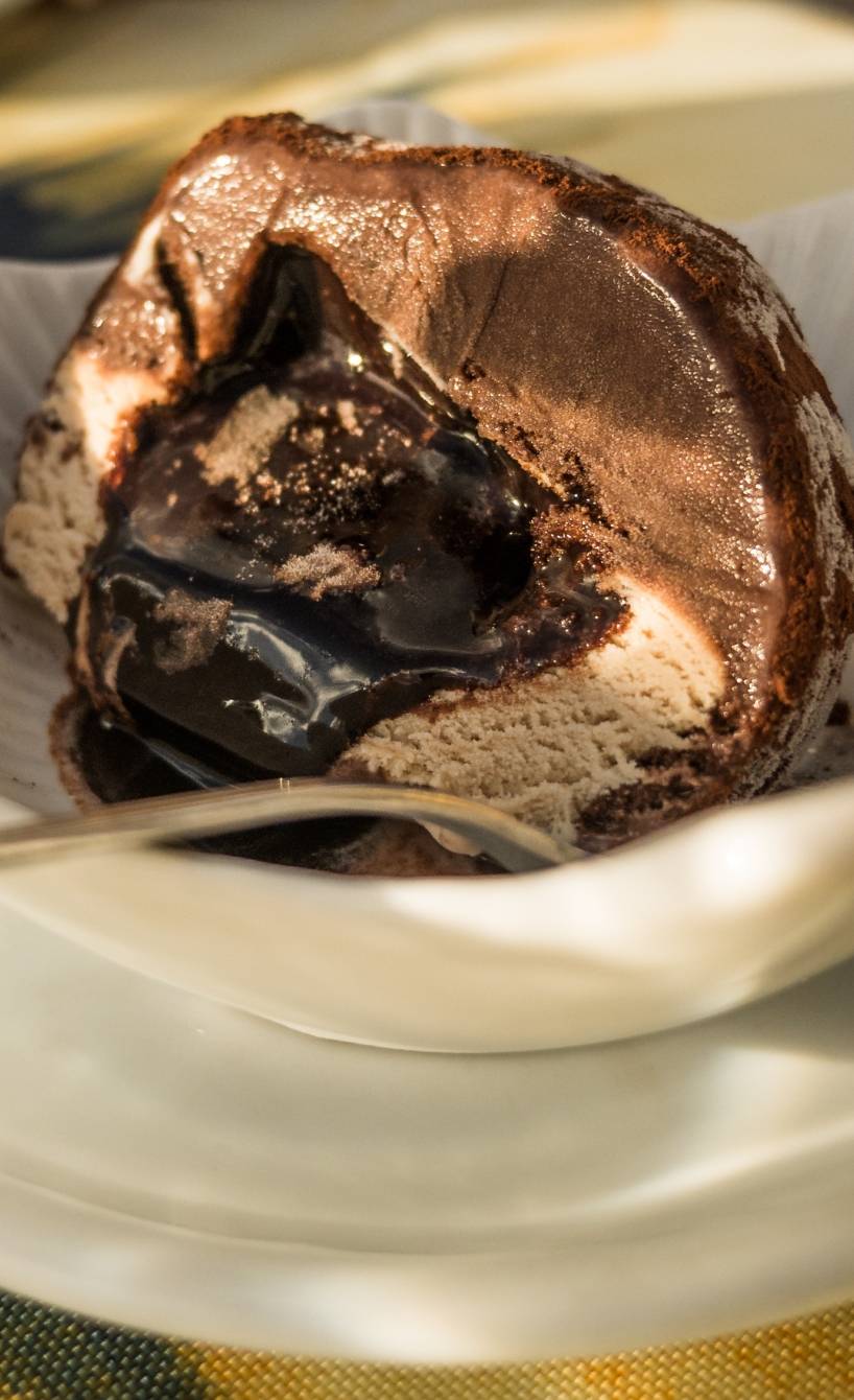 Eine angeschnittene Kugel Tartufo Eis in einer Eisschale, Schokoladensoße fließt heraus