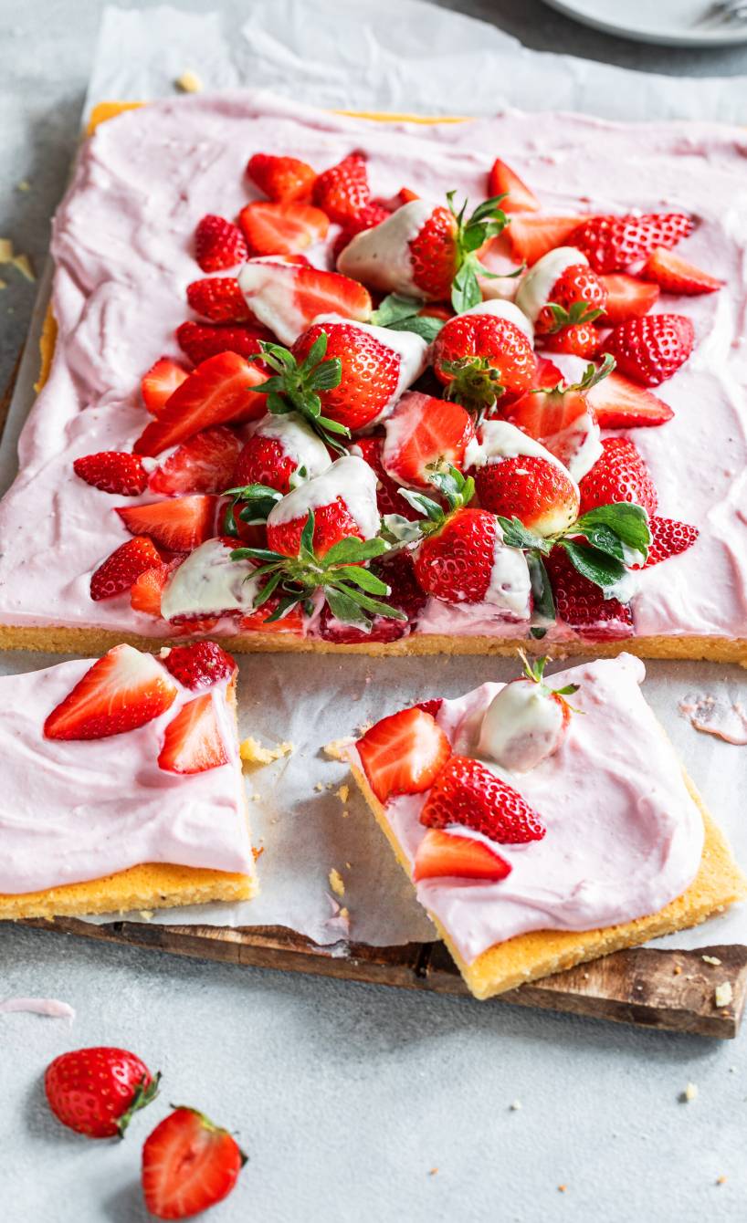 Quark-Erdbeer-Kuchen auf einem Backblech getoppt von teilweise schokolierten frischen Erdbeeren