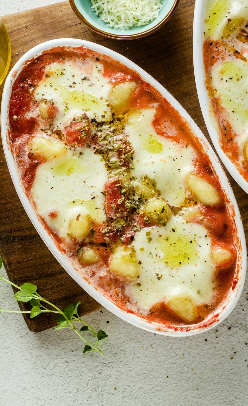 Überbackene Gnocchi alla Sorrentina mit Mozzarella in Tomatensoße in zwei Auflaufformen auf einem Holzbrett