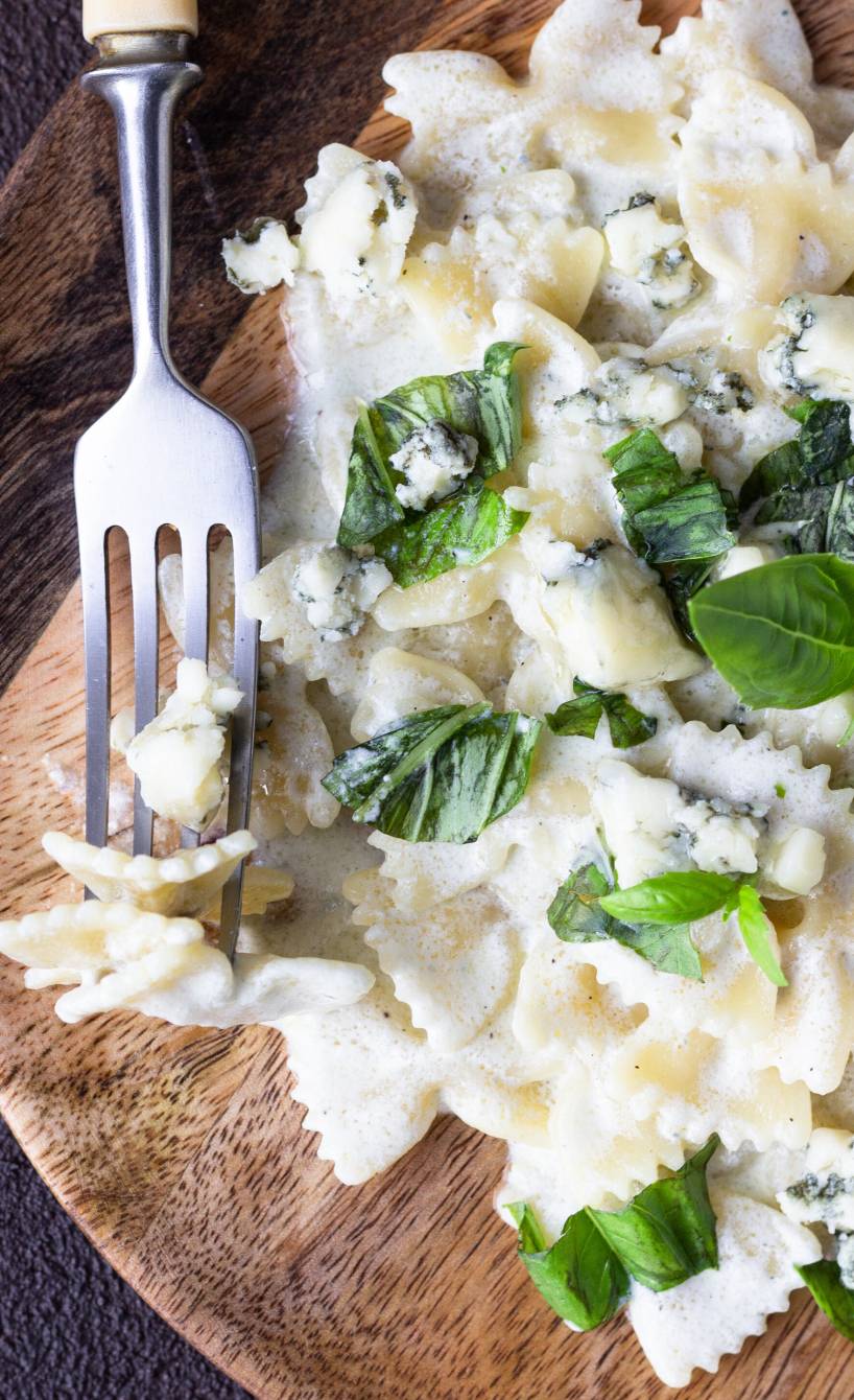 Gorgonzolasauce angerichtet zu Pasta auf einem Holzteller garniert mit frischem Basilikum