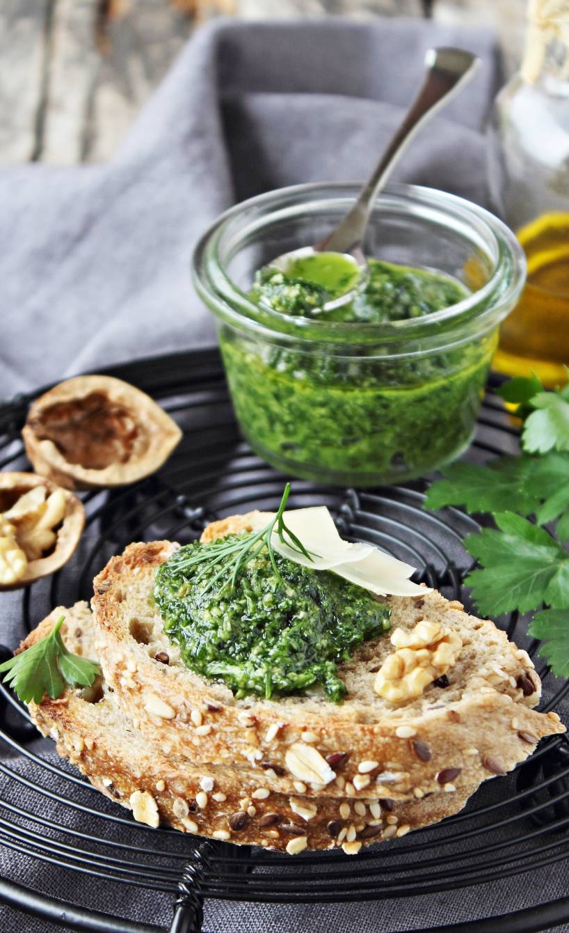 Mangoldpesto auf einem Stück Brot, dahinter ein Glas haltbar gemachtes Pesto