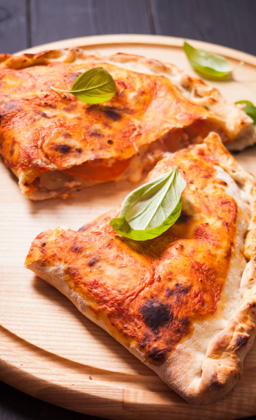 Pizza Calzone halbiert auf einem Holzbrett, Füllung mit Käse gut sichtbar