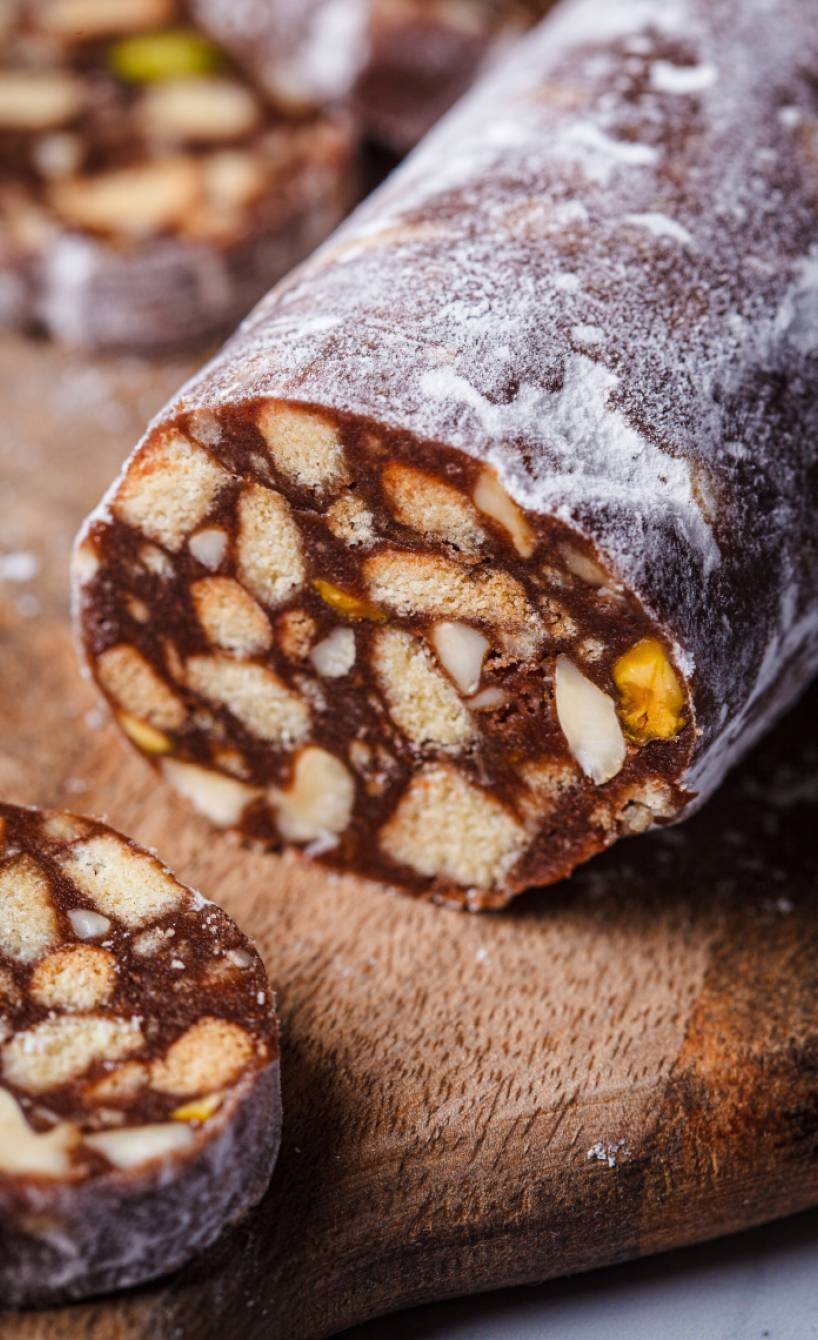 Selbst gemachte Schokosalami mit Keksen und Nüssen angeschnitten auf einem Holzbrett