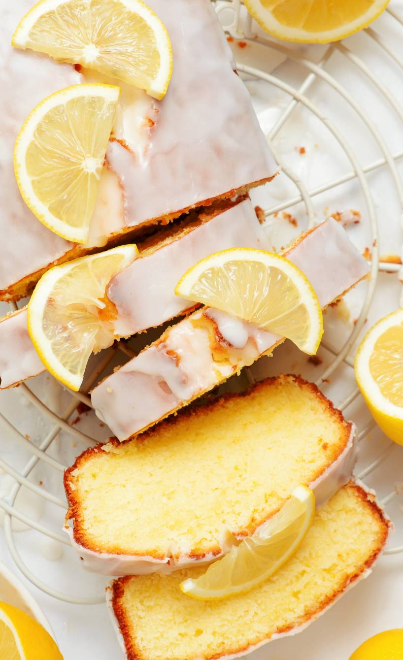 Zitronenkuchen mit Olivenöl aus der Kastenform angeschnitten auf einem Kuchengitter, daneben Zitronen