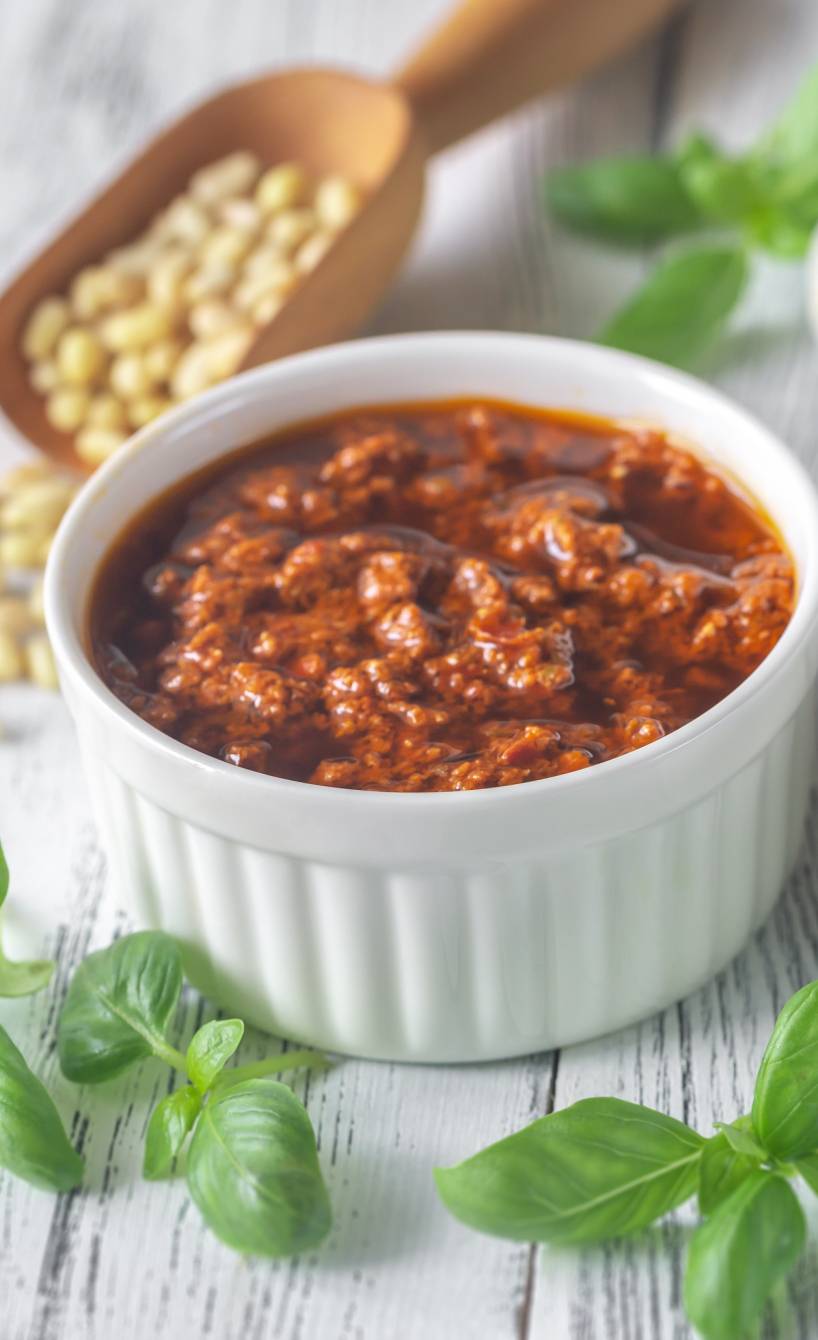 Rotes und grünes Pesto in Keramikschälchen auf einem Tisch, drumherum diverse Pestozutaten Rotes und grünes Pesto in Keramikschälchen auf einem Tisch, drumherum diverse Pestozutaten