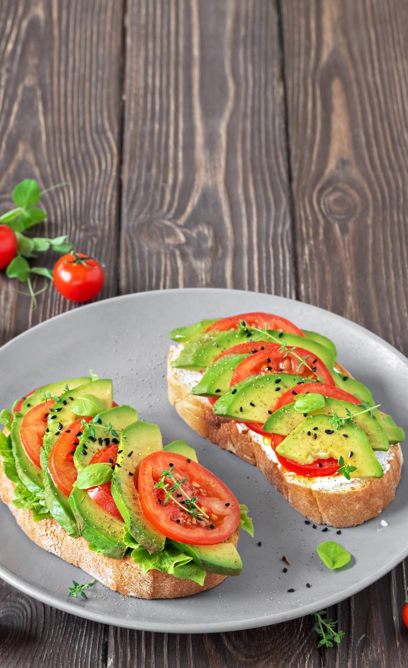 Zwei Avocado-Bruschettas mit Tomaten, veganem Frischkäse und Salat auf einem Teller