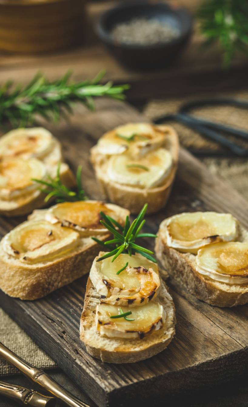 Fünf Bruschettas mit geschmolzenen Ziegenkäsetalern getoppt mit Honig und Rosmarin auf einem Holzbrett