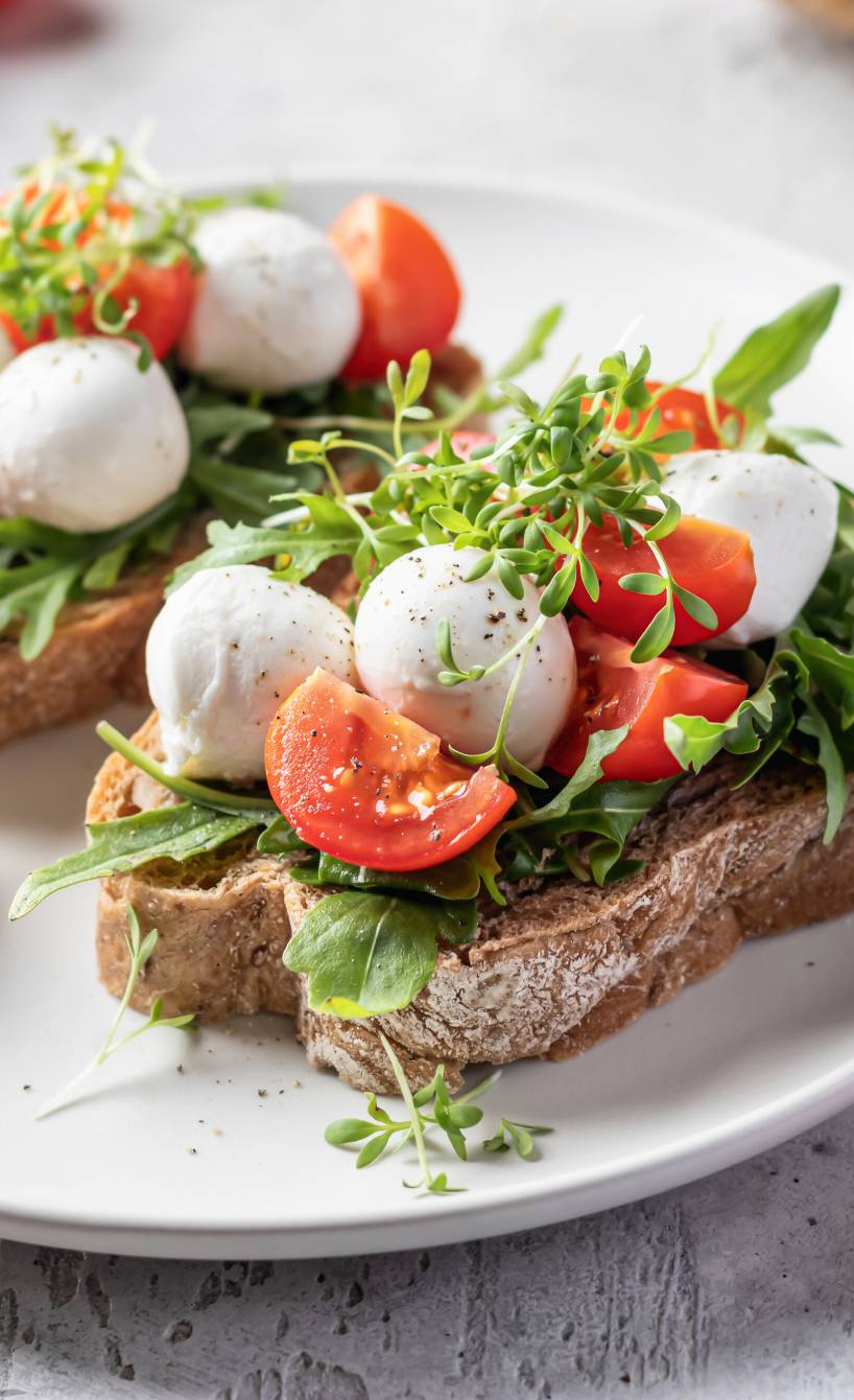 Zwei Bruschettas belegt mit Tomate, Mozzarella und Rucola auf einem Teller Zwei Bruschettas belegt mit Tomate, Mozzarella und Rucola auf einem Teller