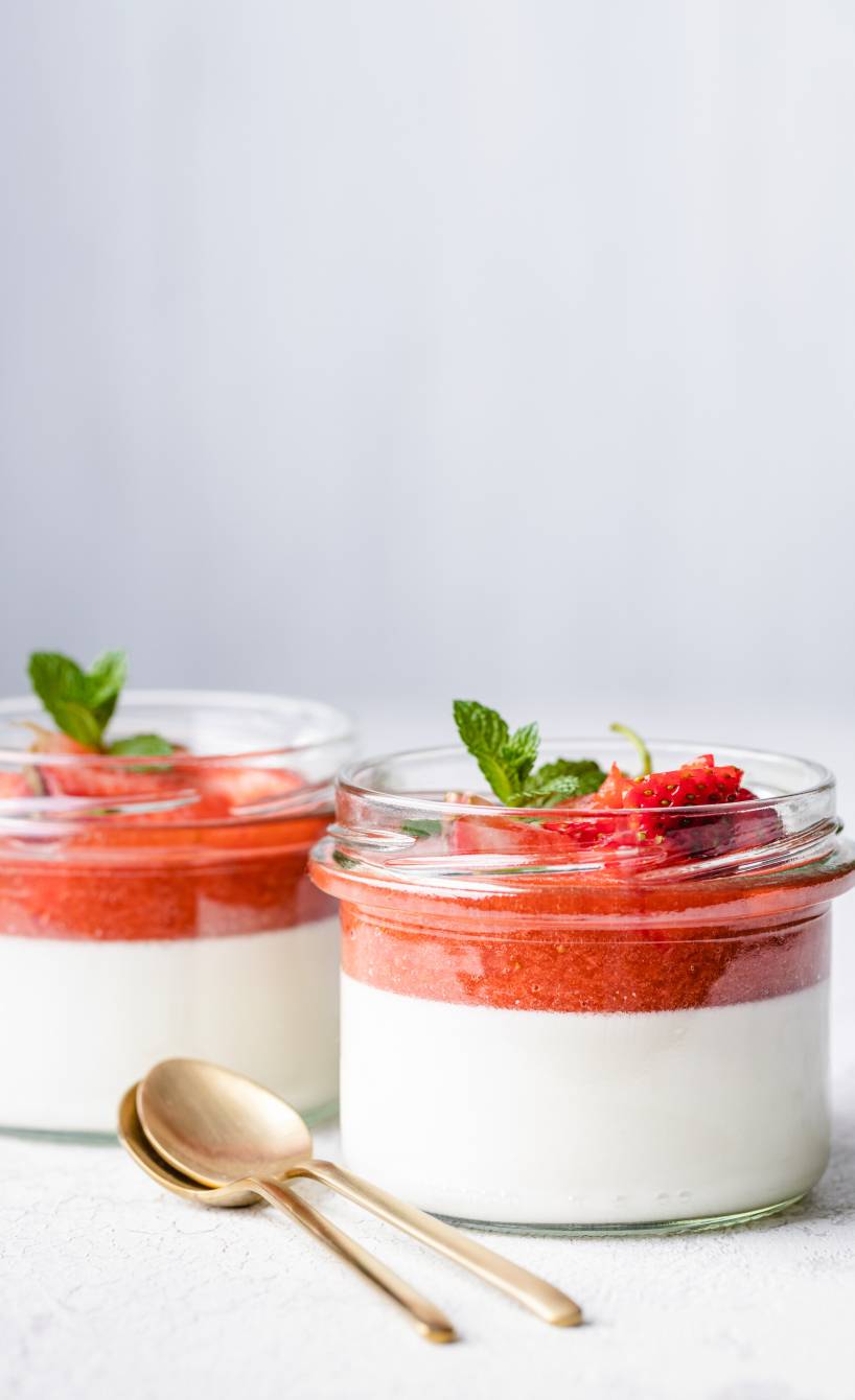 Erdbeer-Panna Cotta geschichtet in zwei Gläser getoppt mit Erdbeerspiegel und Minze auf einem Tisch