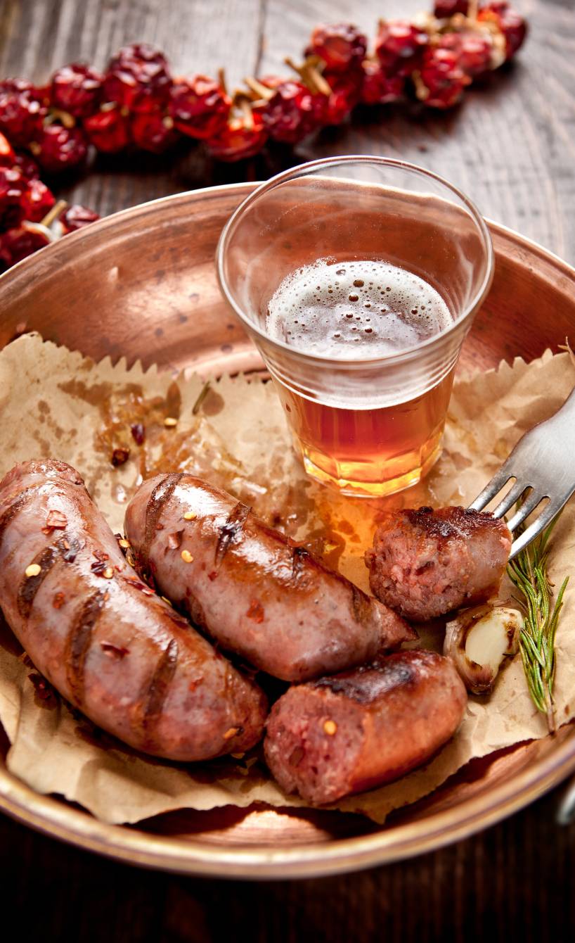 Gegrillte Salsiccia auf einem Tonteller, daneben Knoblauch und Rosmarin