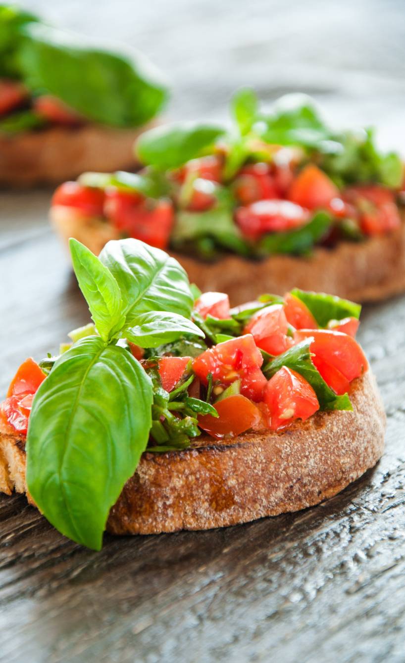 Drei Bruschetta mit frischen Tomaten und Basilikum auf einer Holzplatte