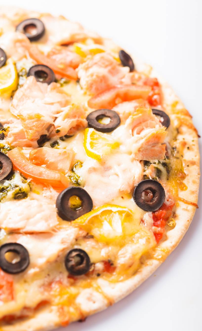 Runde Lachs-Pizza mit Zitrone, Tomaten, Oliven und Mozzarella angeschnitten auf einem Teller