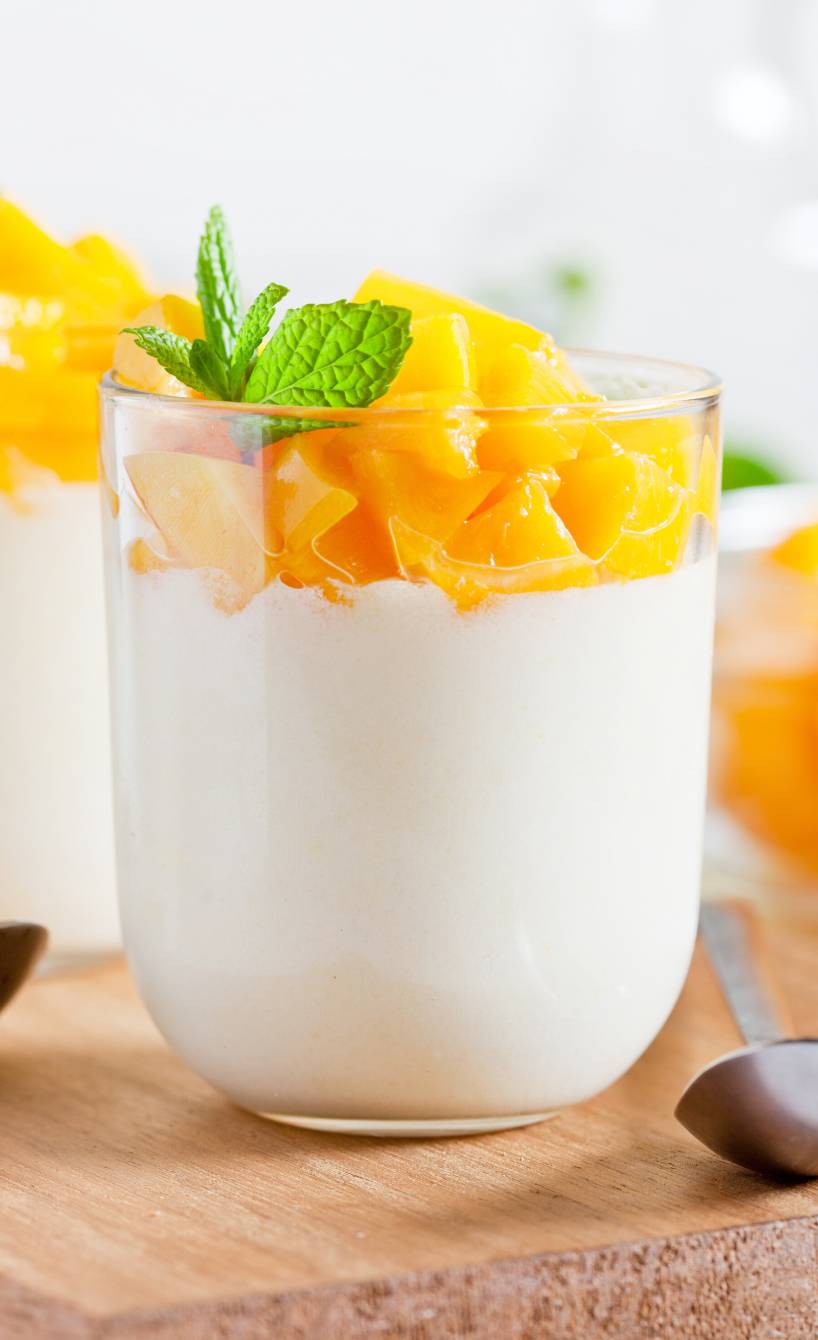 Mango-Panna cotta in zwei Gläsern getoppt von frischer Minze auf einem Tisch