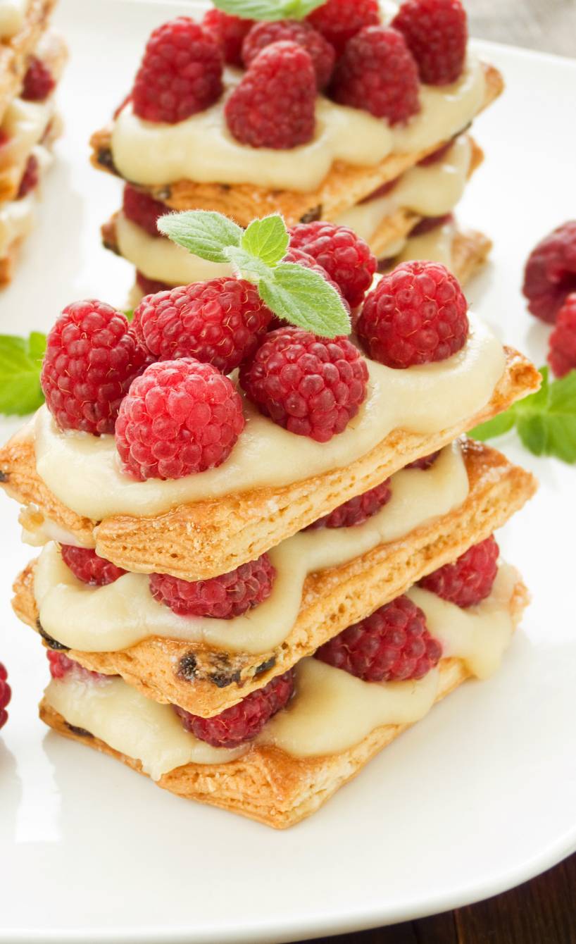 Millefoglie-Torte aus Blätterteigschichten gefüllt mit Vanillepudding-Creme und frischen Himbeeren auf einem Tisch