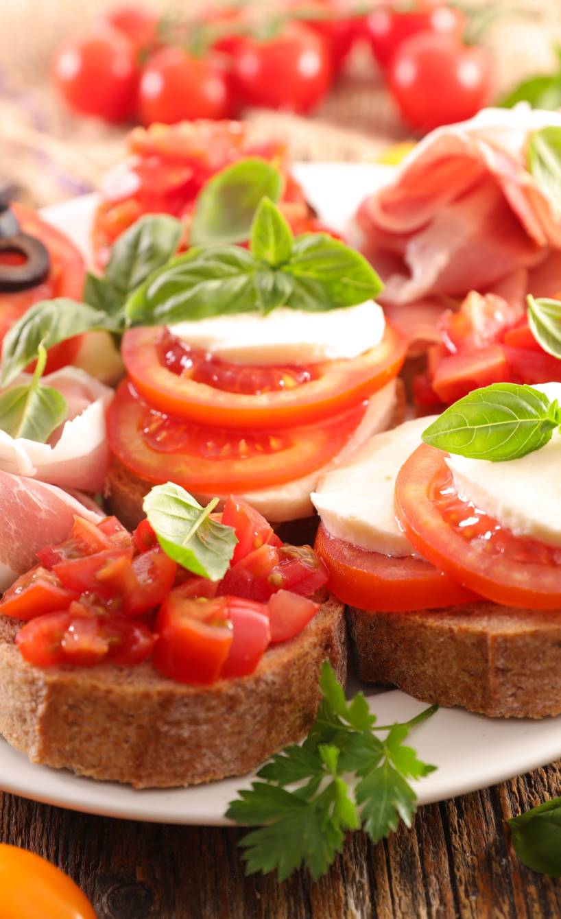 Verschiedene Bruschetta mit Tomate Mozzarella und Schinken belegt als Vorspeise angerichtet auf einer großen Platte