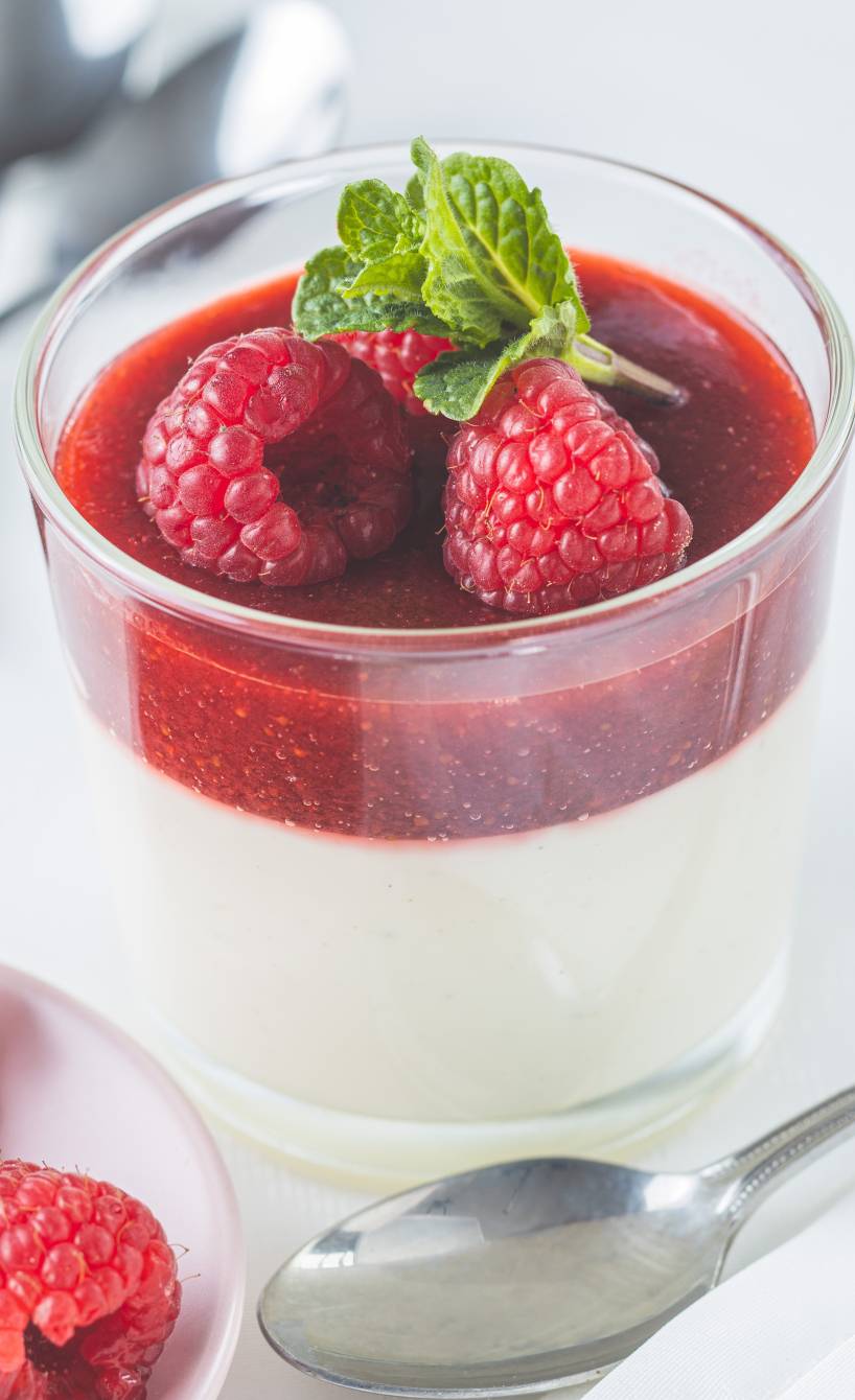 Panna cotta in Dessertgläsern getoppt von Himbeersoße und Minzblättern auf einem Tisch