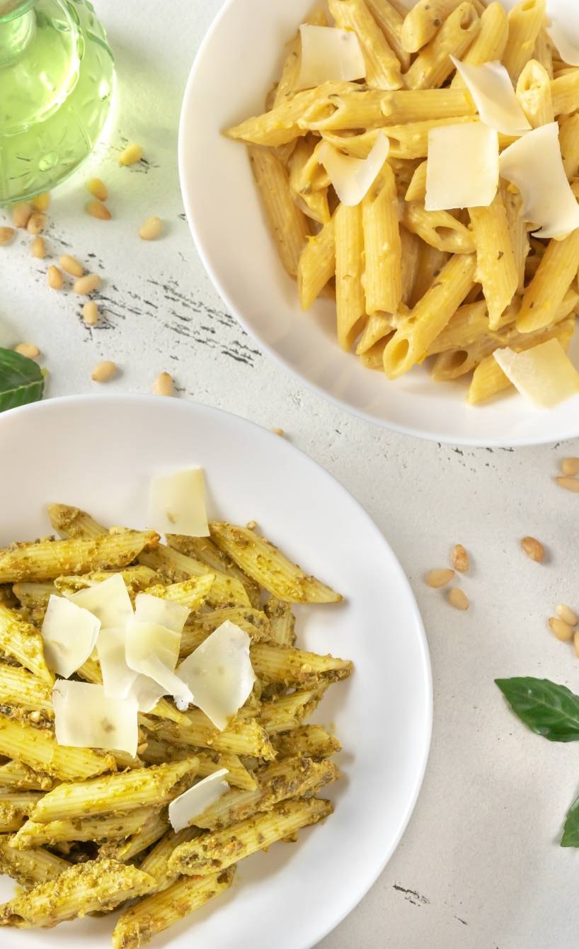 Drei Teller Penne mit jeweils einem anderen Pesto angerichtet, getoppt von Parmesanspänen