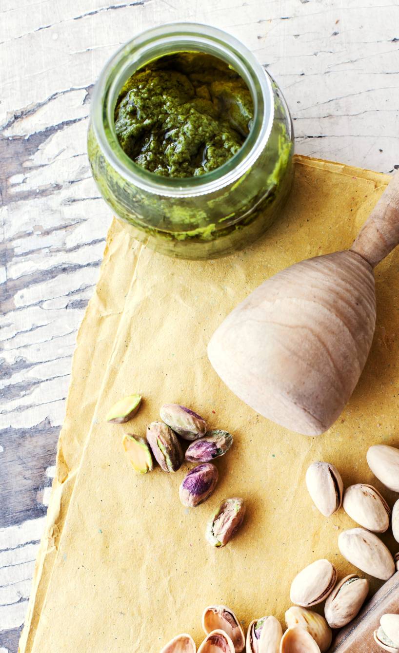 Selbst gemachtes Pistazienpesto in einem Glas, daneben Pistazien auf einem Tisch