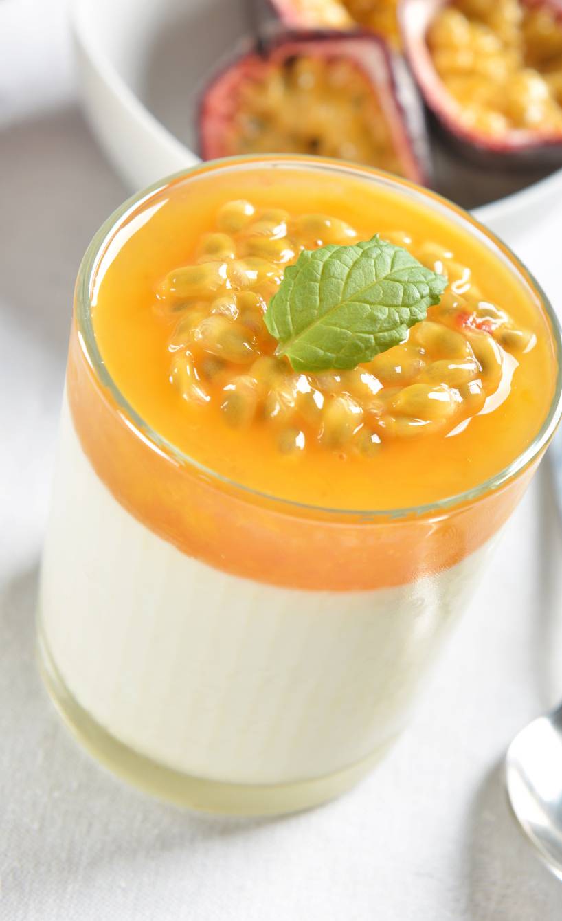 Solero-Panna cotta in einem Glas, daneben halbierte Maracujas auf einem Tisch