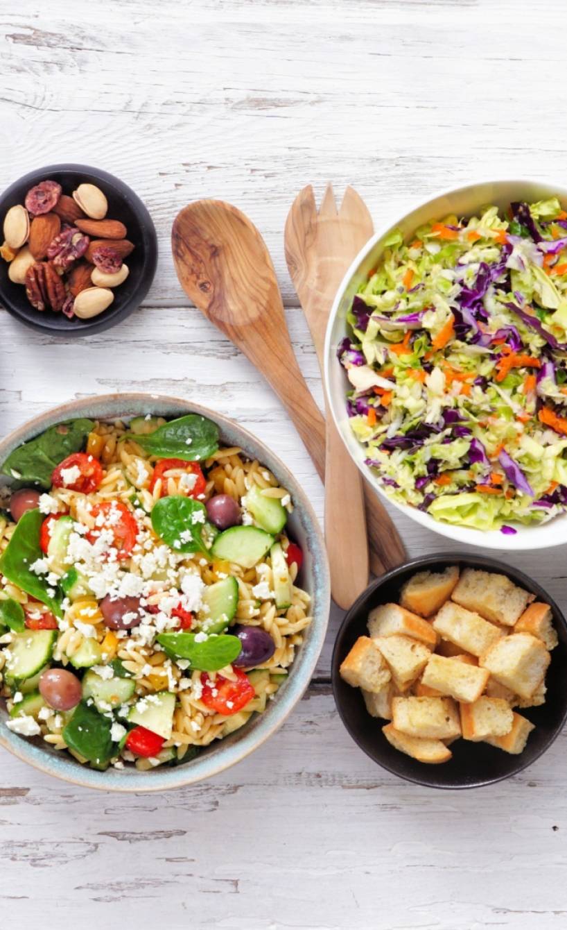 Verschiedene Sommergerichte mit Nudeln und Salat auf einem weißen Holztisch von oben