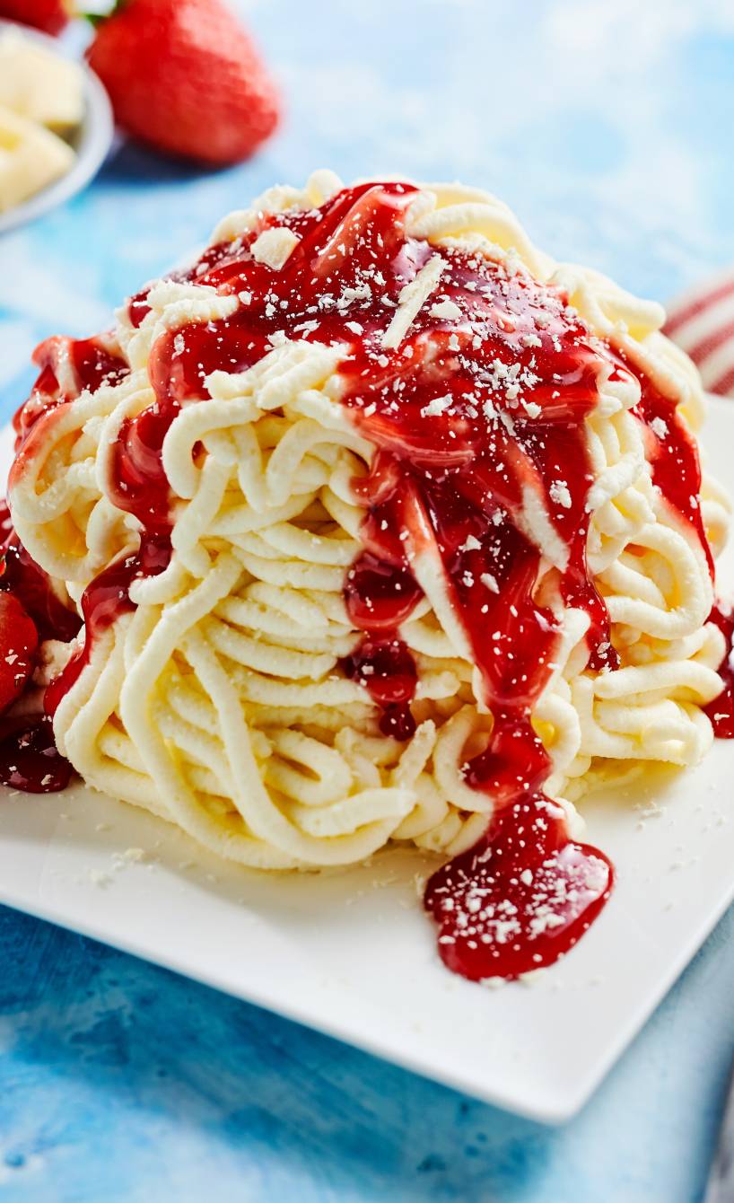 Selbst gemachtes Spagehttieis getoppt mit Erdbeersoße und weißen Schokoladenraspeln auf einem Dessertteller
