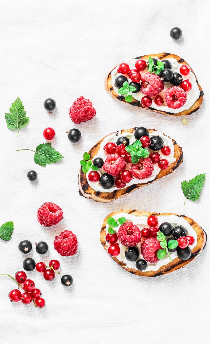 Drei süße Bruschettas getoppt mit Ricotta, Honig, Beeren und Minze auf einem Tisch