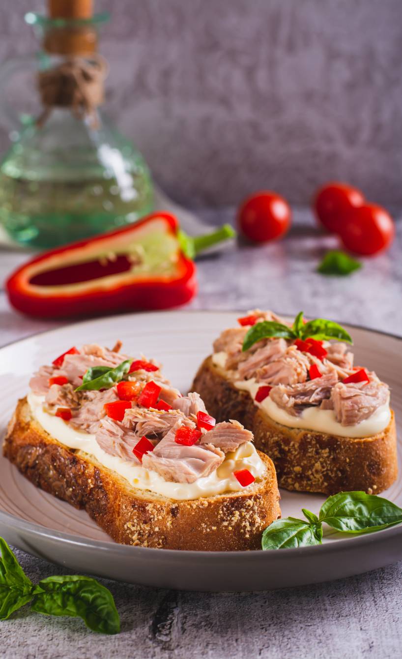 Zwei Thunfisch-Bruschette mkt Frischkäse, Paprika und Tomaten garniert mit Basilikumblättern auf einem Teller