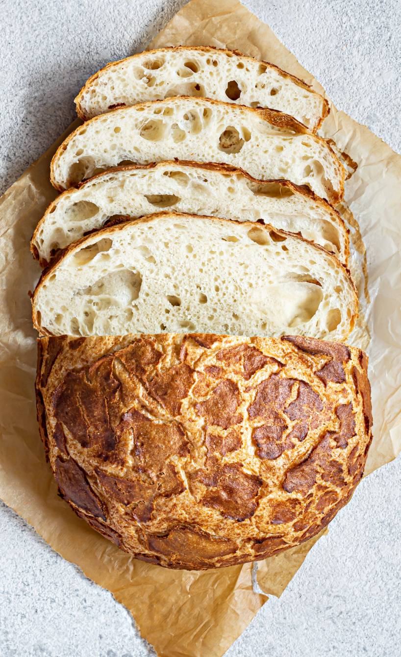 Ein angeschnittener Laib Tigerbrot mit rissiger Kruste auf einem Stück Backpapier