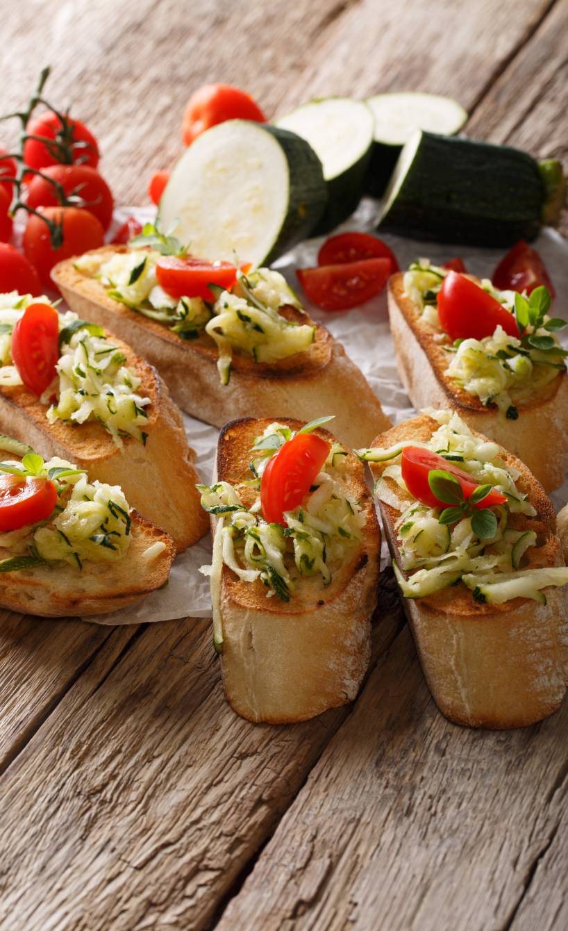 Sechs vegane Zucchini-Bruschettas mit Tomaten auf einem Holztsich