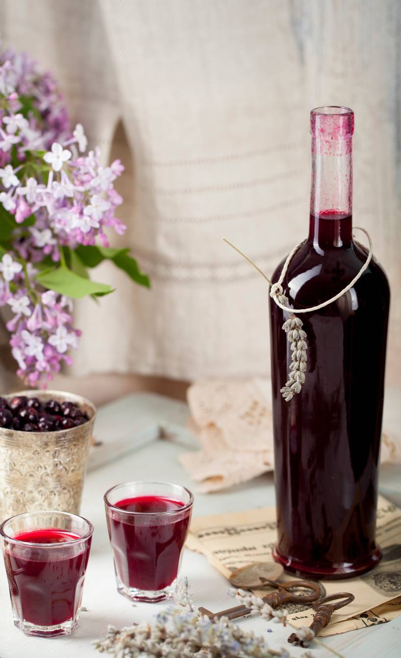 Selbst gemachter Johannisbeerlikör in eine Flasche abgefüllt, daneben zwei Schnapsgläser mit Creme de cassis