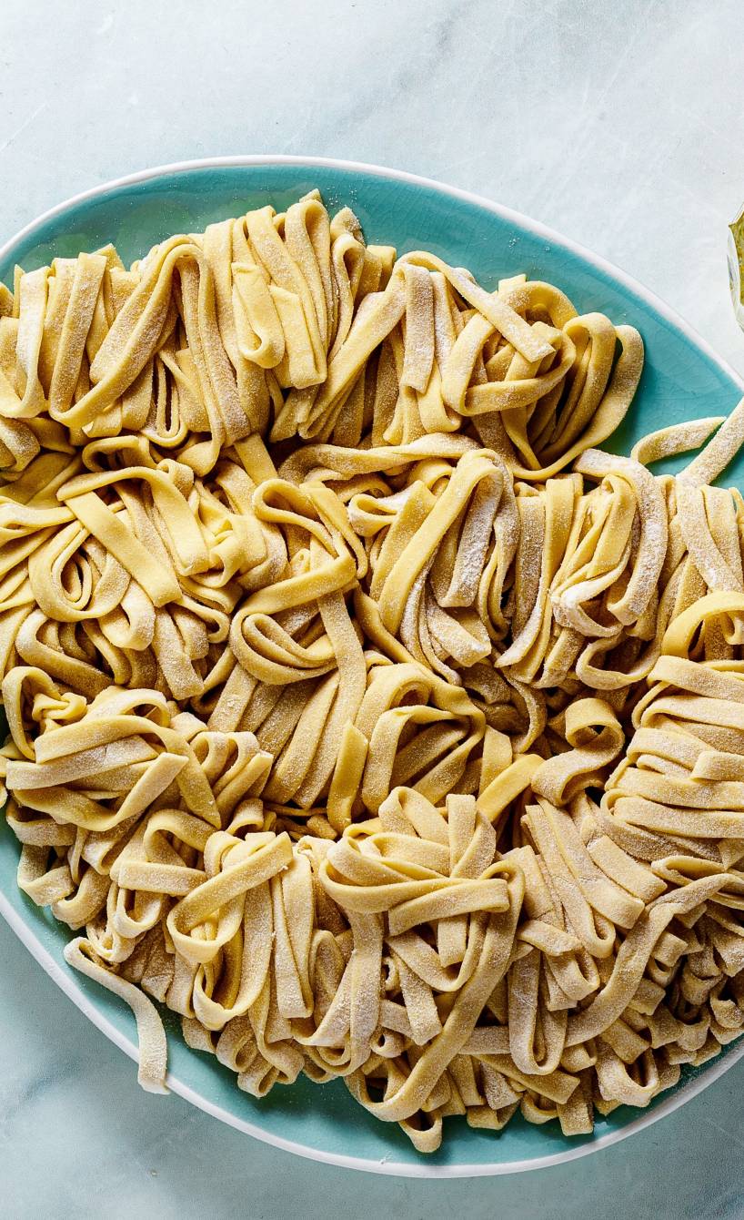 Selbst gemachte glutenfreie Bandnudeln auf einem Teller, daneben Olivenöl und andere Zutaten von oben auf einem Marmortisch Selbst gemachte glutenfreie Bandnudeln auf einem Teller, daneben Olivenöl und andere Zutaten von oben auf einem Marmortisch
