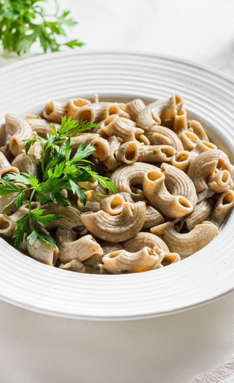 Glutenfreie Nudeln auf einem Teller, daneben Sauce und geriebener Käse auf einem Tisch