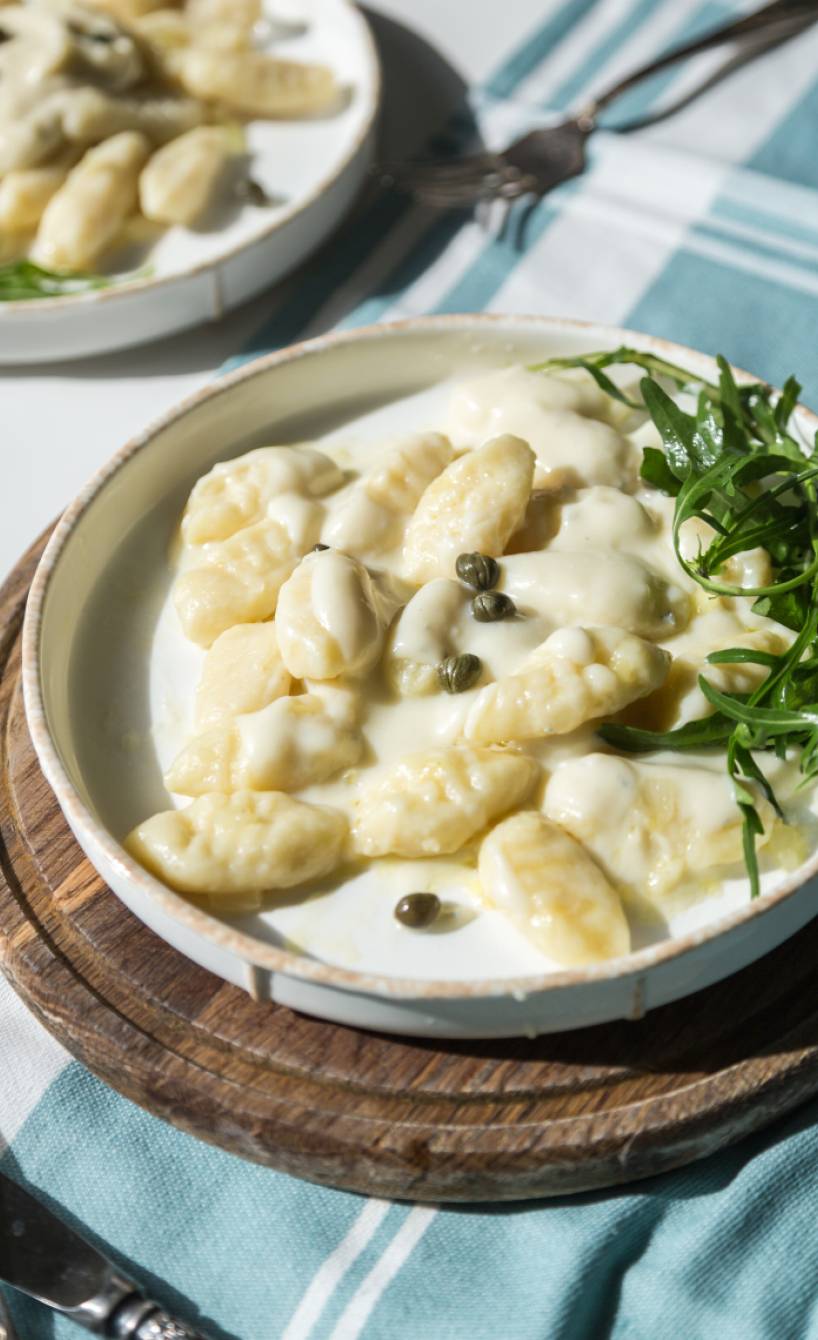 Gnocchi mit Asiago-Käsesoße auf einem Teller angerichtet mit Rucola und garniert mit Kapern