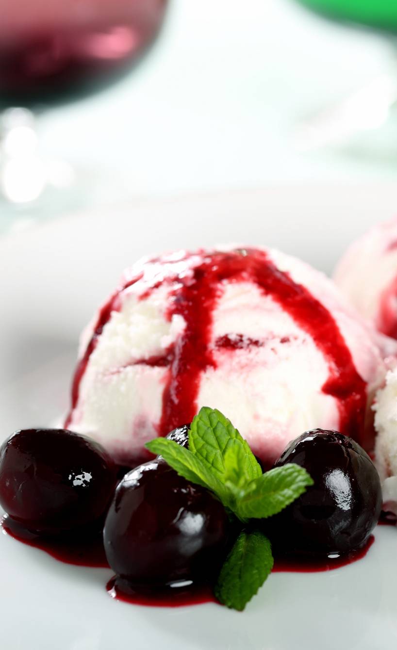 Drei Kugeln Amarena-Eis auf einem Dessertteller garniert mit Amarena-Kirschen und Minze